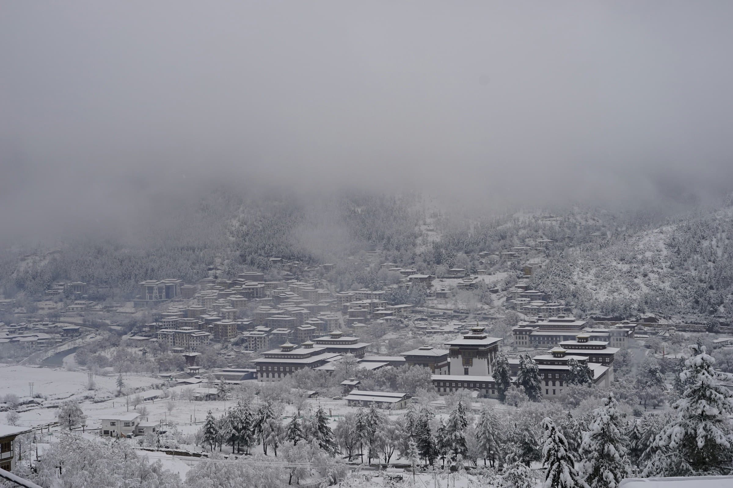 Thimphu valley under snow and low cloud, Tashichho Dzong in the foreground.